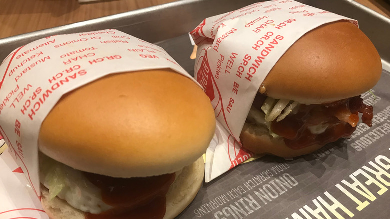 Two hamburgers from Fatburger wrapped with paper on a plastic tray.
