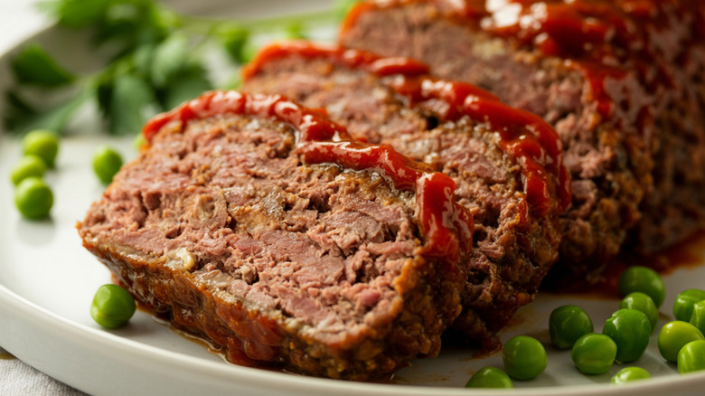 Ketchup-topped sliced meatloaf is plated with peas.
