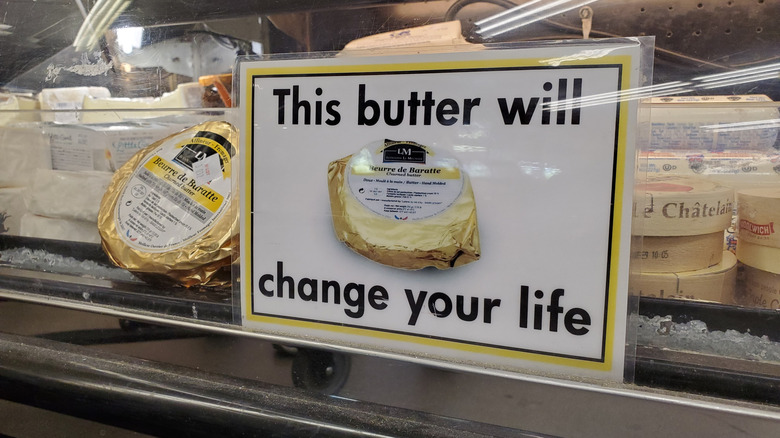 A round package of Beurre de Baratte next to a sign with the words "This butter will change your life" on a display case of butter