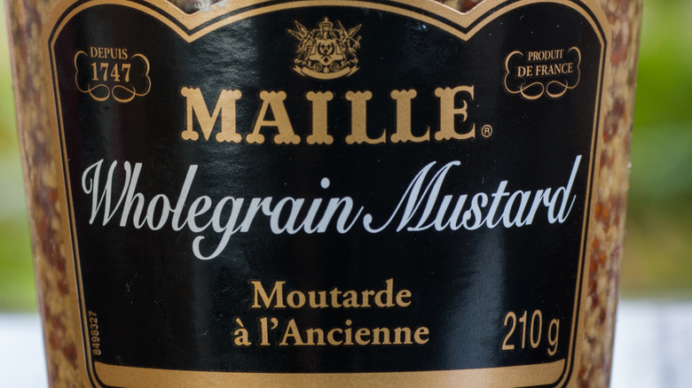 The label on a glass jar of Maille brand whole-grain mustard, with gold and white text on a black background