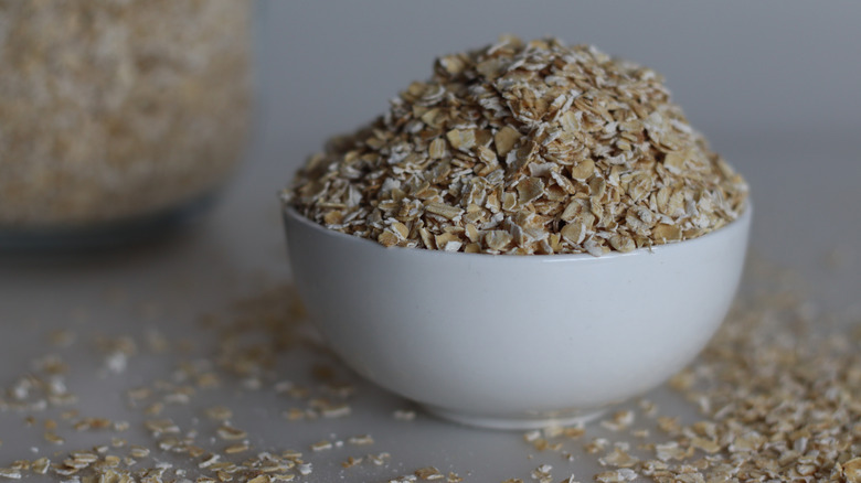 White bowl filled with quick-cooking oats on a gray table top with scattered oats around it