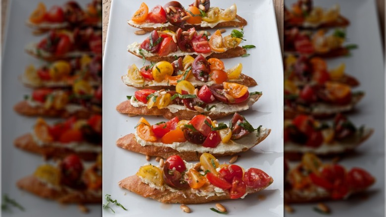 A row of tomato crostinis with feta and tomato topping on a white plate