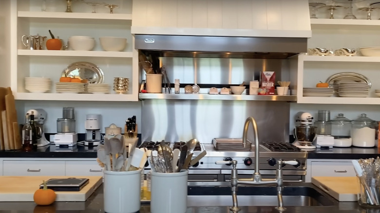 A partial view of Ina Garten's barn kitchen, featuring her open cabinets, stove, sink, appliances, and various cooking utensils