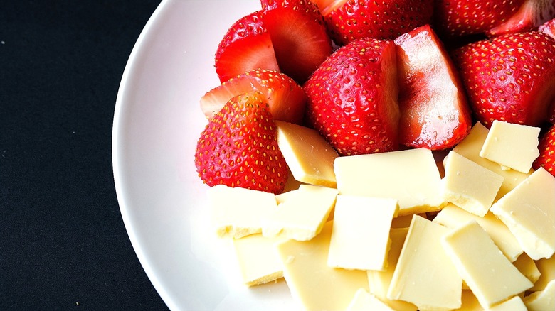 Closeup of halved fresh strawberries and broken white chocolate on a white plate