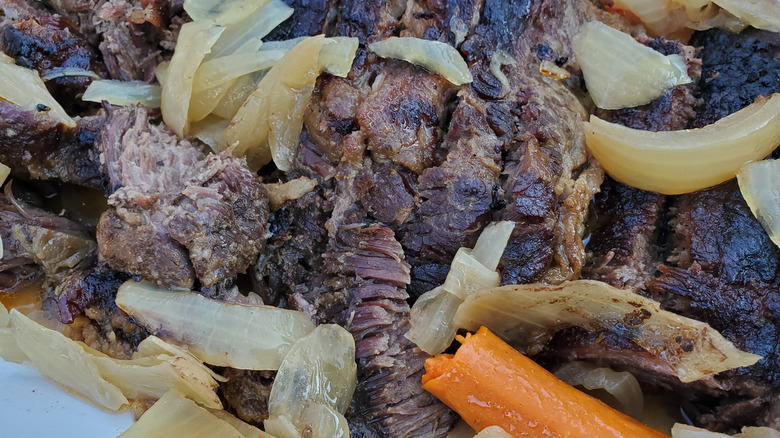 slices of homemade brisket in a pan with carrot and onions