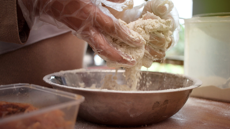 A person breads chicken over a bowl.