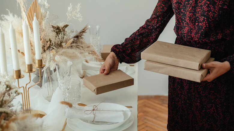 A person placing gifts in brown paper packaging on a nicely set dining table.