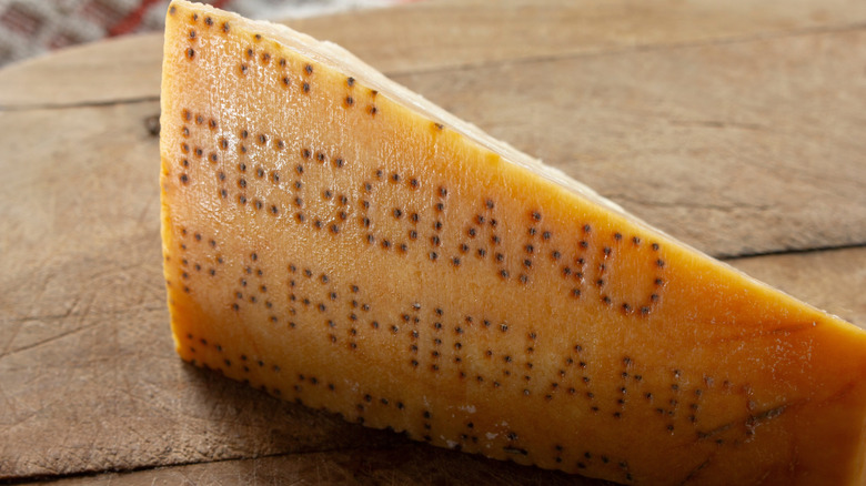 A wedge of parmesan on a wooden table, the rind engraved with "REGGIANO" and "PARMIGIANO"