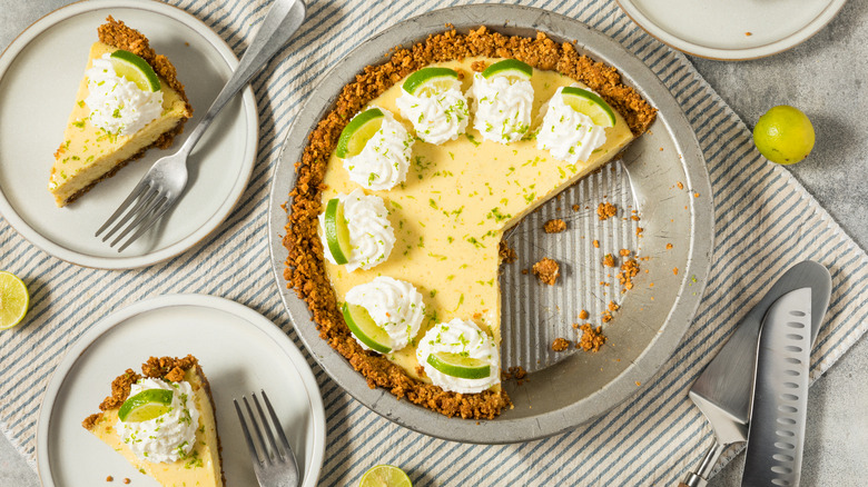 Key lime pie with a graham cracker crust in a pan next to individual slices on plates