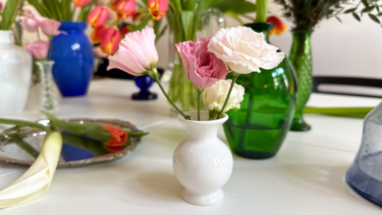 Pink and white flowers in small vases on table next to place setting