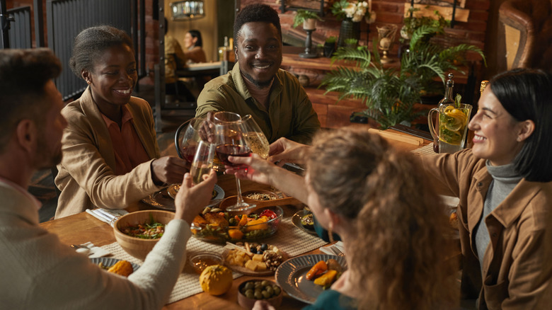 Five people sitting around a dinner table, toasting with wine and champagne