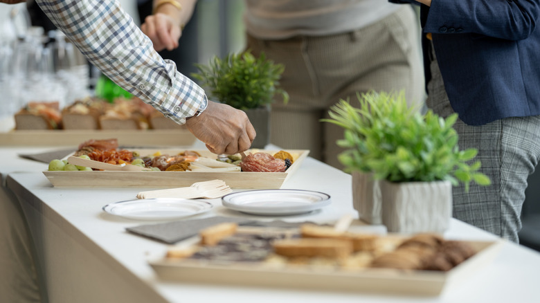 Man's arm and hand taking food from tray on buffet