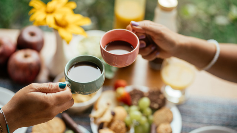Two women's hands holding pink and green coffee mugs in a toast