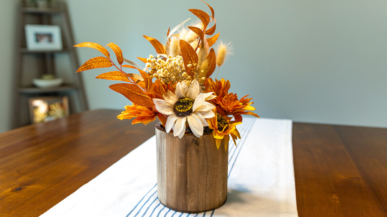 Orange leaves and beige flowers in a wooden vase on a white table runner