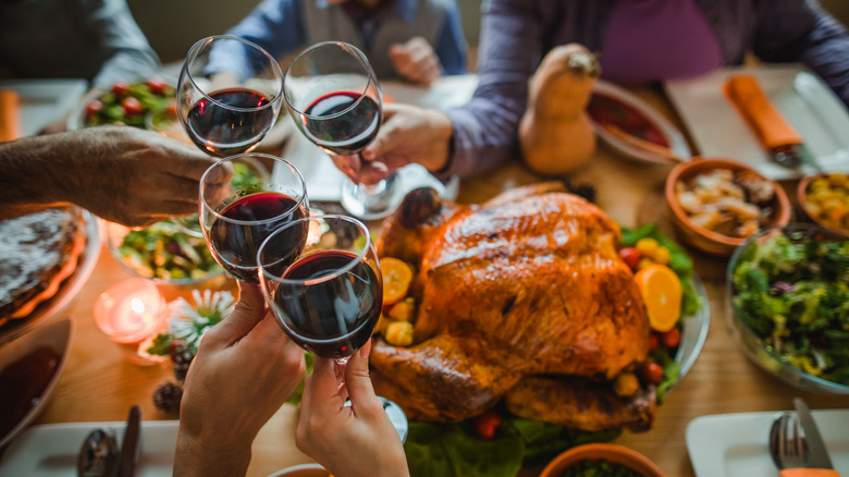 A Thanksgiving table features a turkey as people's hands are seen toasting with red wine above the bird.
