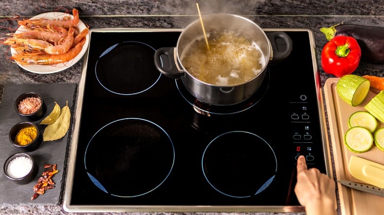 An induction stovetop with a boiling pot on it and plates of ingredients surrounding it