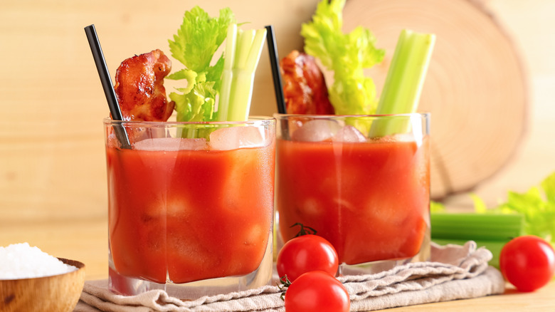 A pair of bloody Marys garnished with celery and bacon.