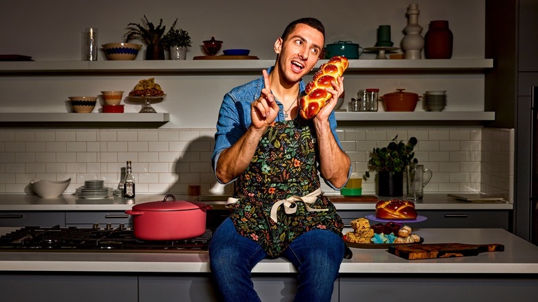 Instagram chef Jake Cohen sitting on countertop holding a loaf of challah like a phone