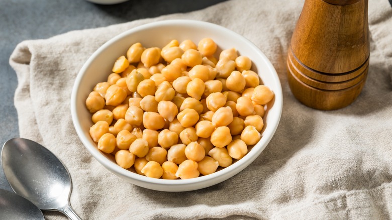 A bowl of cooked chickpeas on a tea towel, surrounded by a pepper grinder and a spoon.