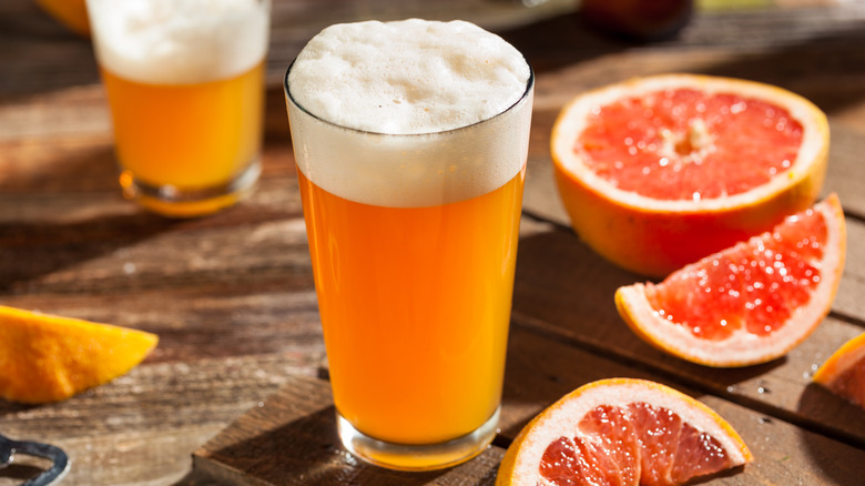 A sudsy beer on a wooden table with grapefruit halves and wedges arranged in the frame.