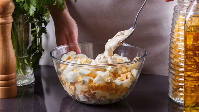 A person making a ham and egg salad in a bowl.