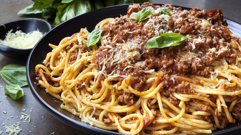 a close up of spaghetti with creamy meat sauce and basil leaves