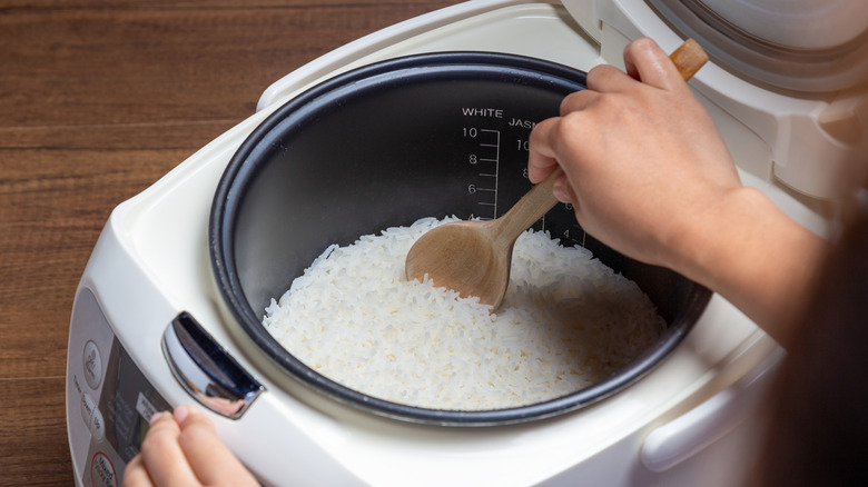 A person scoops rice out of a rice cooker with a wooden spoon