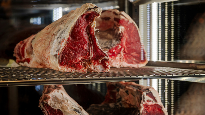 Large cuts of meat dry aging in a large fridge.