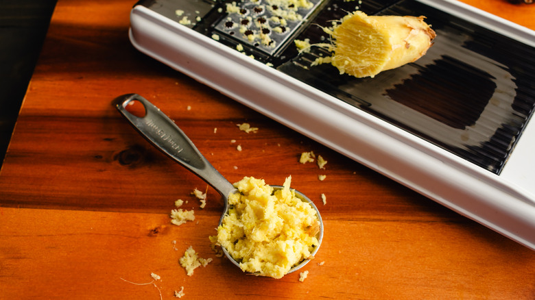 One tablespoon of fresh grated ginger on wooden counter.