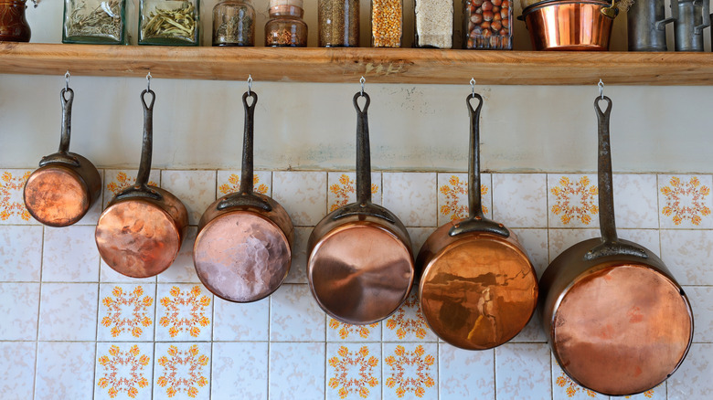 Copper pans hanging from small to large from wood shelf holding jars of herbs and spices