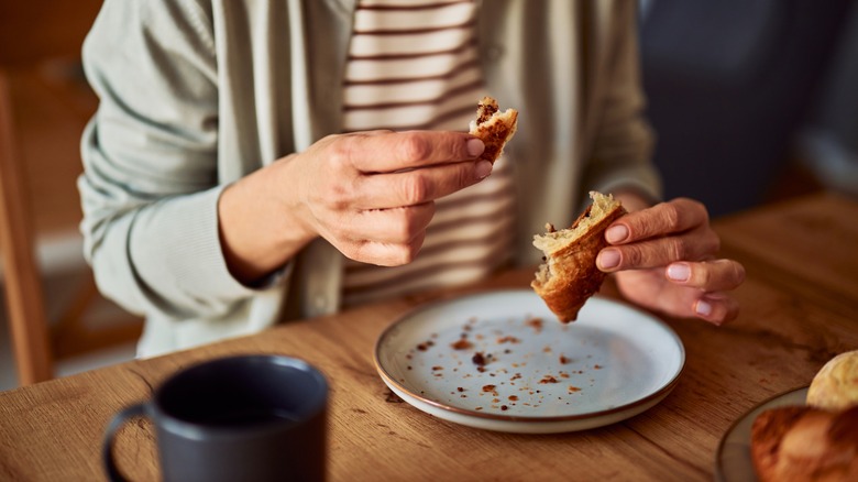 hands tearing off a bite size piece of croissant over a plate