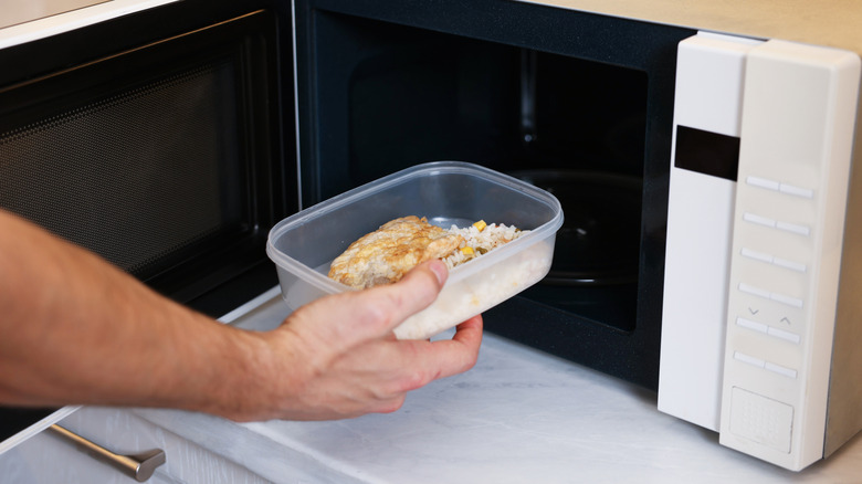 person putting food container into microwave