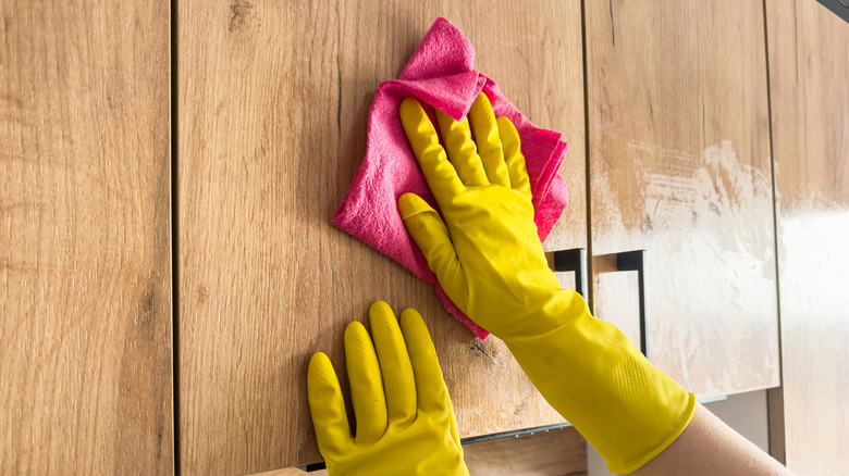 Person wiping down wooden cabinets with a cloth