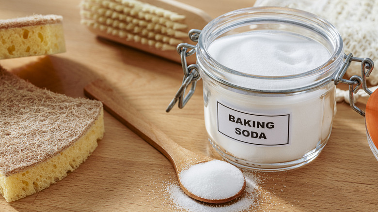 A container of baking soda next to cleaning tools