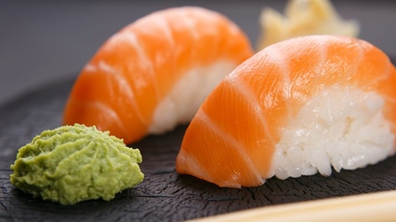 A mound of wasabi next to two fresh pieces of sushi made with salmon on a black plate