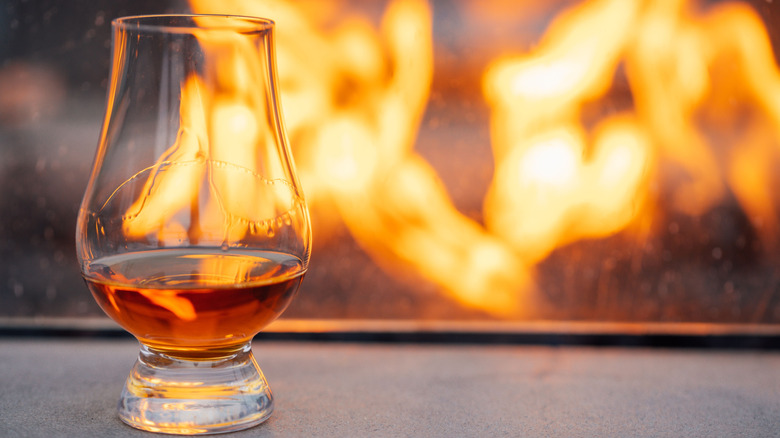 A Glencairn glass, designed for whiskey, holds the spirit in front of a fire.