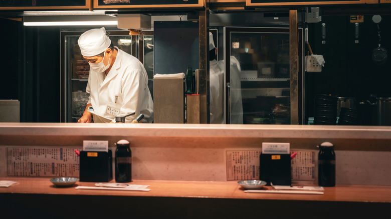 A sushi chef prepares sushi behind a counter