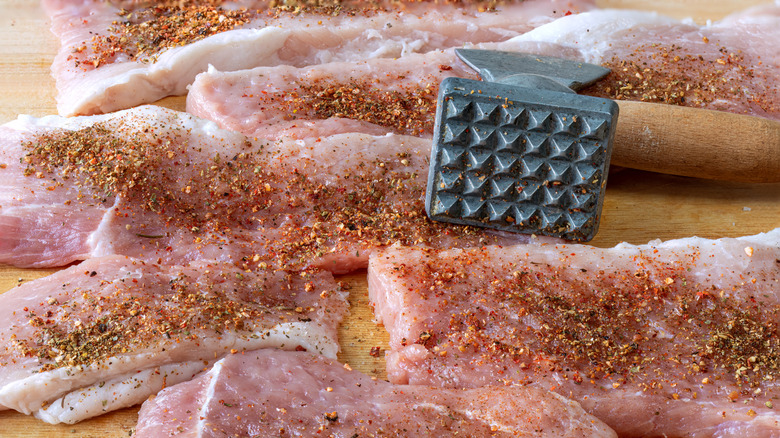 Seasoned cuts of meat after being tenderized with a meat mallet resting on the cutting board