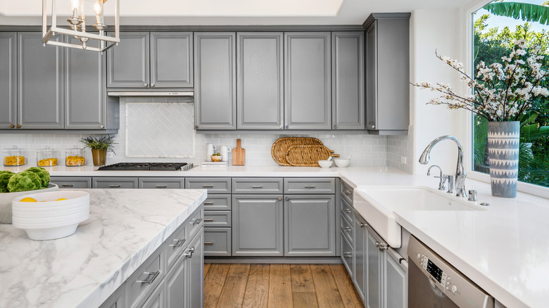 A bright kitchen has white, marble countertops and lots of cabinets.