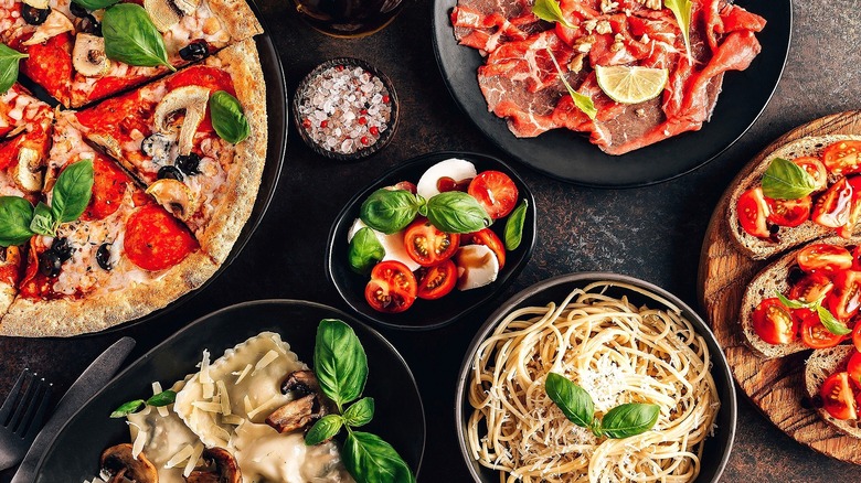 Assorted Italian dishes like pizza, pasta, and crostini on black plates