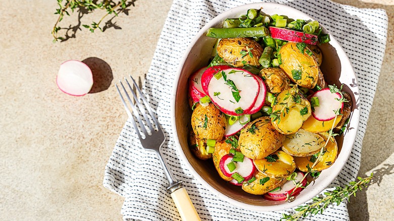 Herbed potato salad with chopped green beans and sliced radishes in a white bowl