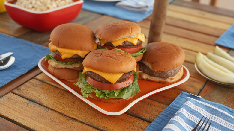Four burgers are arranged on a plate on an outdoor table.