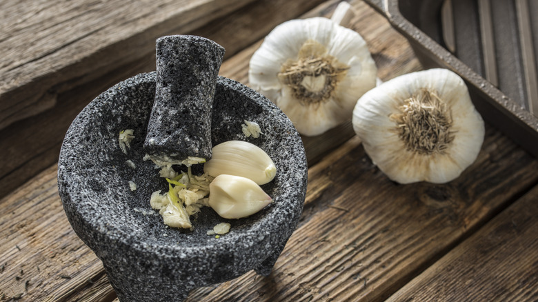 Garlic cloves in a mortar with a pestle on a wooden table.