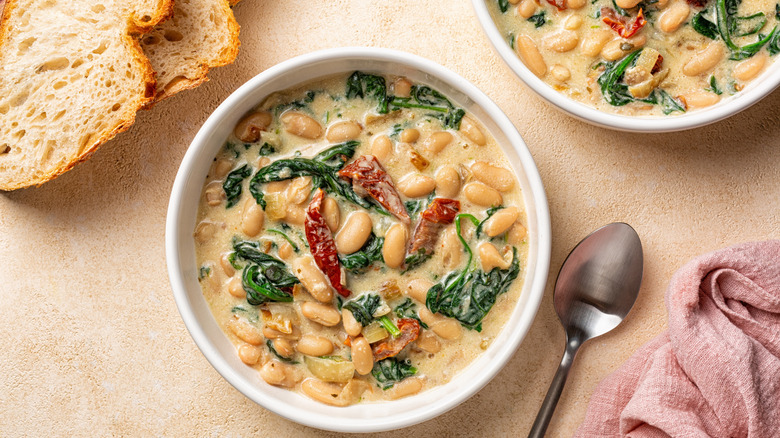 Bowls with Tuscan butter beans stew with spinach and sun-dried tomato, vegan cream. Vegetarian homemade meal.