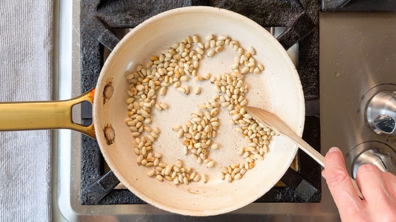 Stirring pine nuts toasting in skillet on stovetop