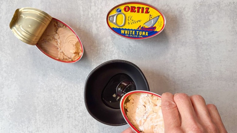 Pouring off oil from canned tuna to small black bowl
