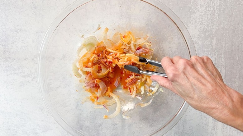 Adding shaved fennel and red onion to vinaigrette with tongs in glass bowl