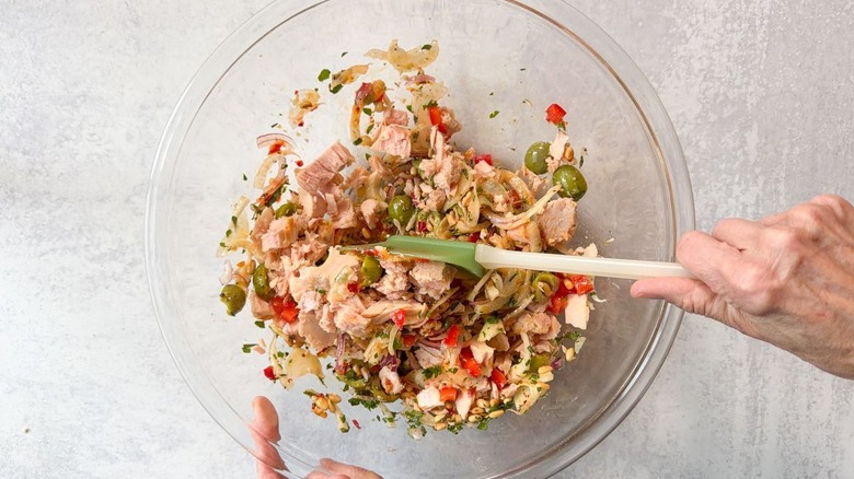 Folding flaked canned white tuna into Italian-style tuna salad in large glass bowl