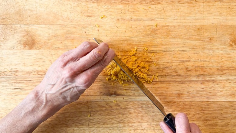 Mincing lemon zest with chef's knife on cutting board