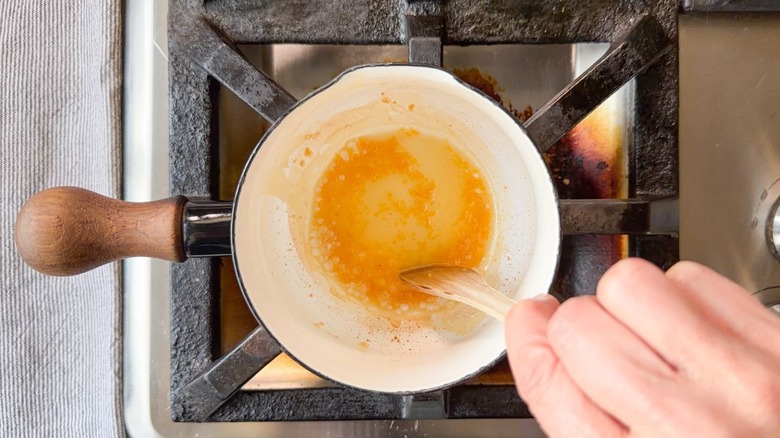 Stirring quick-preserved lemon in small saucepan with wooden spoon